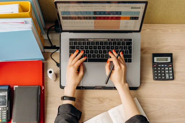 Hands typing on a laptop beside folders and a calculator on a wooden desk
